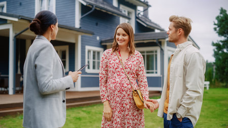 Professional Realtor Showing a Hot Property Location to a Young Successful Couple. Female Real Estate Agent with Tablet Walking with Family to the House. Newの写真素材