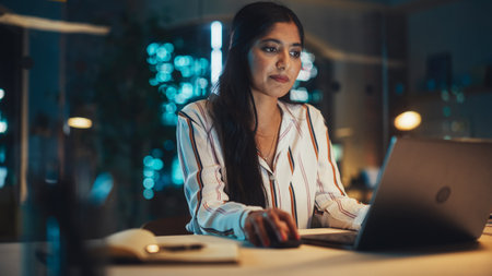 Portrait of a Beautiful Indian Female Working on Laptop Computer in a Company Office at Night. Young...