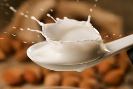 Close up of pouring milk into spoon with almonds in the background.の写真素材