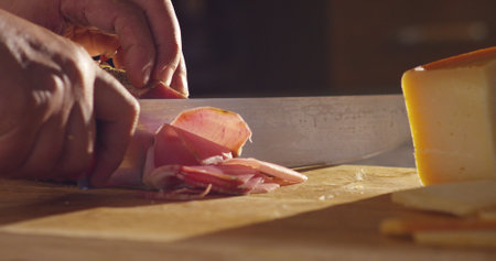 chef cutting prosciutto on a wooden board with knifeの写真素材