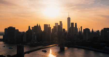 Iconic New York City Landscape Over East River with Skyscrapers, Brooklyn Bridge, Cars and Ferry Boats. Cinematic Evening Urban Skyline with Sunset and Lightly Clouded Skyの写真素材