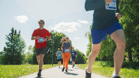 Portrait of a Group of People Participating Together in a Marathon and Running Through a Park Trail. Joggers Giving their Best to Achieve the Finish Line in a Friendly Raceの写真素材