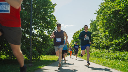 Portrait of a Group of People Participating Together in a Marathon and Running Through a Park Trail. Joggers Giving their Best to Achieve the Finish Line in a Friendly Raceの写真素材