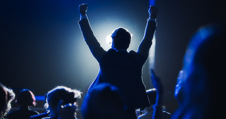 Young Excited Man Ecstatic About Winning the Coveted Business Person of the Year Award. Man Jumping After Winning the Event Category. Handsome Specialist Celebrating and Cheering a Colleague on Stage.の写真素材