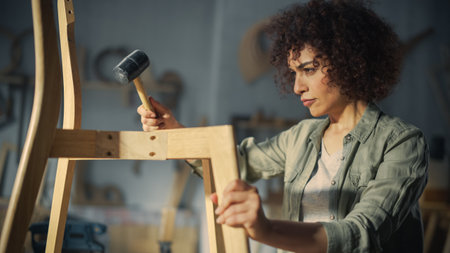 Close Up Portrait of a Beautiful Multiethnic Carpenter Assembling a Wooden Chair. Professional Furniture Designer Working in a Studio in Loft Space with Tools on Walls.の写真素材