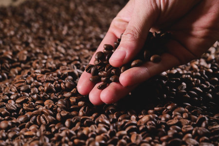 Roasted coffee beans in hand on brown background. Selective focus.の写真素材