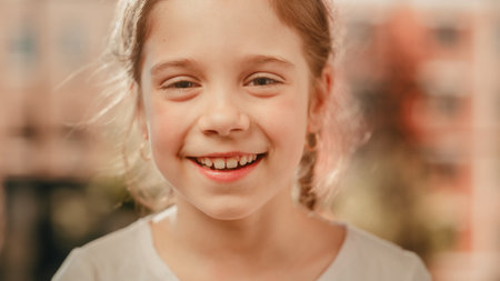 Close Up Portrait of an Adorable Little Girl with Brown Eyes and Hair Looking at Camera, Smiling Happily. Smart Talented Girl Laughing and Having Fun at Home. Soft Bokeh Background.の写真素材