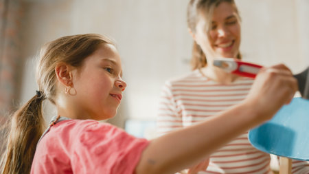 Moving in and Home Renovations: Happy Mother Painting Vintage Furniture Chair Daughter Tries to Help Her. Cheerful Young Family Make Apartment Cozy with Art, Color. Smiles and Happiness.の写真素材