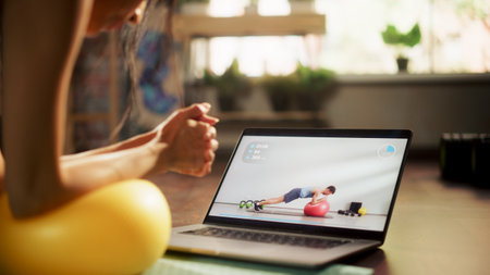 Strong Beautiful Asian Fitness Girl in Workout Uses Laptop for Online Exercise, Does Plank Yoga...