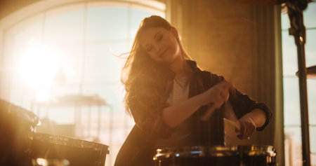 Close Up Portrait of an Expressive Drummer Girl Playing Drums in a Loft Music Rehearsal Studio Filled with Cinematic Contre-Jour Light. Rock Band Music Artist Learning a New Drum Solo.の写真素材