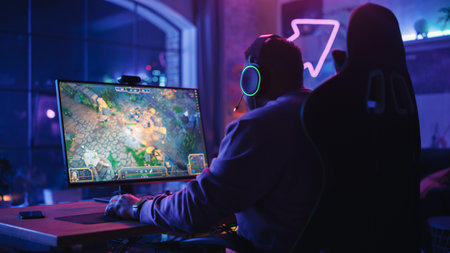 Successful Gamer Playing and Winning in PvP RPG Strategy Video Game in Which Players Fight in a Battle Royale Tournament on Personal Computer. Stylish Man Celebrating Victory in Cozy Room at Home.の写真素材