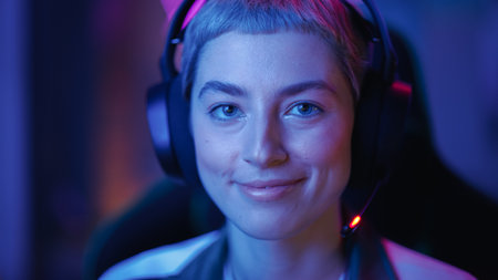 Portrait of a Female Gamer Playing Online Video Game on Computer. Close Up of Stylish Woman in Headphones Enjoying Leisure Time, Smiling and Posing for Camera. Cyber Gaming Stylish Retro Neon Room.の写真素材