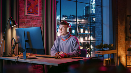 Young Handsome Man in Headphones Using Computer in Stylish Loft Apartment at Night. Creative Male...