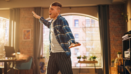Portrait of Handsome Stylish Young Man Dancing in Casual Clothes, Having Fun at Home in Loft Apartment. Recording Funny Viral Videos for Social Media. Medium Shot.の写真素材