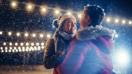 Romantic Winter Snowy Evening: Ice Skating Couple Having Fun on Ice Rink, Spin and Dance. Pair Skating Outdoors. Portrait of Young People, Boyfriend and Girlfriend in Love, Smile, Magical Wintertimeの写真素材