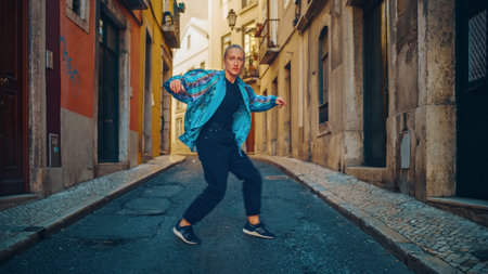 Beautiful Young Adult Woman in Stylish Clothes Actively Dancing Hip Hop on the Street of an Old Town in a City. Scene Shot in an Urban Environment on an Quiet Small Town Street.の写真素材
