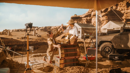 Archaeological Digging Site: Two Great Adventurers on Treasure Hunt Open Chest with Unspeakable Treasures, Celebrates Their Succers by doing High-Five. Ancient Civilization Hidden Gold Foundの写真素材