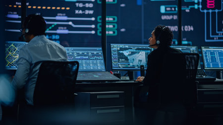 Professional IT Technical Support Specialists and Software Programmer Working on Computers in Monitoring Control Room with Digital Screens with Server Data, Blockchain Network and Surveillance Maps.の写真素材