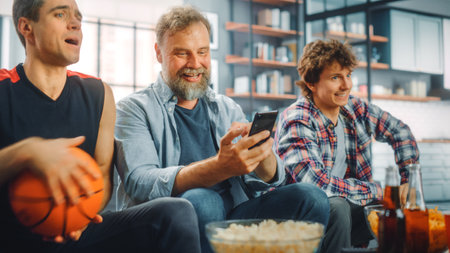 At Home Three Fans Sitting on Couch Watch Basketball Game on TV, Use Smartphone App for Checking...