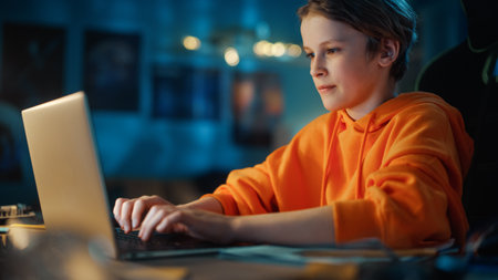 Smart Young Boy Using Laptop Computer in a Dark Cozy Room at Home. Happy Teenager Browsing Educational Research Online, Chatting with Friends, Studying School Homework.の写真素材