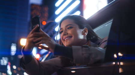 Excited Female is Looking Out of the Window from Backseat of a Car at Night. Woman Taking Photos and...