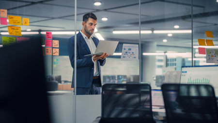 Young Confident Businessman Using Laptop Computer in Modern Office. Stylish Manager in a Suit Working on Commercial, Financial and Marketing Projects. Sales Specialist Browsing Internet, Emails.の写真素材
