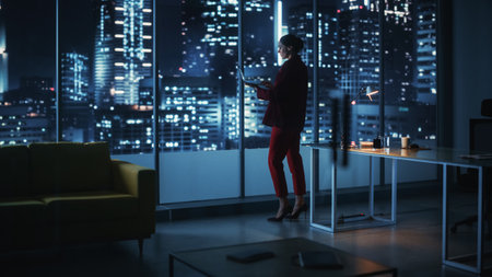 Successful Caucasian Businesswoman Wearing Stylish Suit Holding Laptop Standing in Big City Night Office. Female CEO Managing Environmental, Social and Corporate Governance for e-Commerce Projectの写真素材