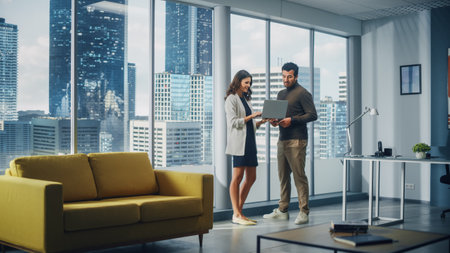 Successful Corporate CEO and Investment Manager Talking, Using Laptop Computer while Standing in Big City Office. Two Successful Diverse People Brainstorm Their e-Commerce Software Investment Strategyの写真素材