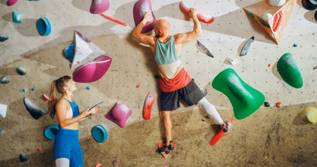 Rock Climbing Instructor Giving Lesson to a Beginner on a Bouldering Wall in a Gym. Female Athlete...