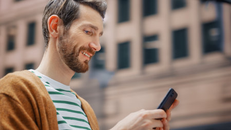Street Shot: Portrait of Caucasian Man Using Smartphone in the Big City. Creative Professional Using Mobile Phone App for e-Commerce Online Shopping. Blurred Background.の写真素材