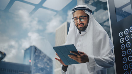 Successful Muslim Businessman in Traditional White Kandura Riding Glass Elevator to Office in Modern Business Center. Man Using Tablet Computer. Saudiの写真素材