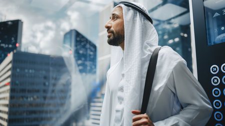 Successful Happy Muslim Businessman in Traditional White Kandura Riding Glass Elevator to Office in...
