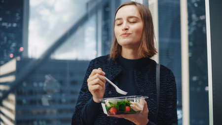 Portrait of a Confident Young Female Riding Glass Elevator to Office in Modern Business Center and Eating Healthy Salad with Vegetables. Happy Managerの写真素材