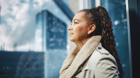 Successful Black Adult Female Riding Glass Elevator to Office in Modern Business Center. Beautiful African American Manager Looking at Downtownの写真素材