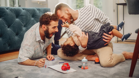 Loving LGBTQ Family Playing with Toys with Adorable Baby Boy at Home on Living Room Floor. Cheerful Gay Couple Nurturing a Child. Concept of Diverseの写真素材