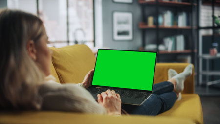 Beautiful Caucasian Specialist Working on Laptop with Green Screen Mock Up Display at Home Living Room while Lying on a Couch Sofa. Freelance Femaleの写真素材