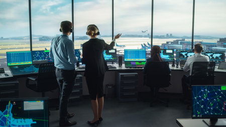 Female and Male Air Traffic Controllers with Headsets Talk in Airport Tower. Office Room is Full of Desktop Computer Displays with Navigation Screensの写真素材