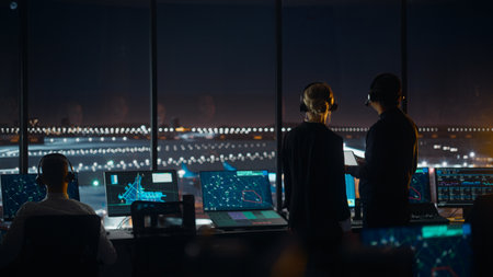 Female and Male Air Traffic Controllers with Headsets Talk in Airport Tower at Night. Office Room...