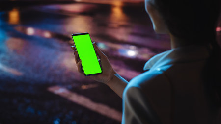 Beautiful Woman using Chroma Key Smartphone while Walking Through Night City Street Full of Neon Light. Female Using Green Screen Mobile Phone. Overの写真素材
