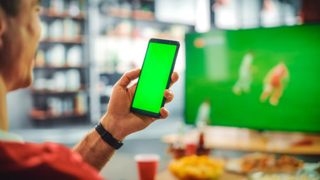 At Home Joyful Soccer Fans Sit on a Couch Watch Green Screen Chroma Key Screen. Friends Cheer for Favourtite Football Sports Team to Win Championship. Over the Shoulderの写真素材