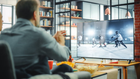 At Home Ice Hockey Fans Sitting on a Couch Watch Game on TV, Cheer when Favourtite Sports Team to Win the Championship. Screen Shows Professional Players During World Cup. Over the Shoulderの写真素材