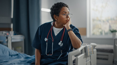 Hospital Ward: Portrait of Sad, Tired Black Nurse Sitting on a Bed, Holding Her Head in Sorrow for all the Patients that Couldnt Be Saved in Pandemicの写真素材
