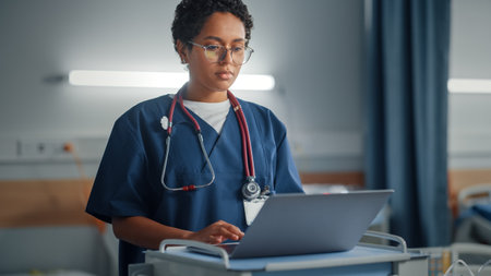 Hospital Ward: Professional Smiling Black Female Head Nurse or Doctor Wearing Stethoscope Uses Medical Computer. In the Background Patients in Beds Recovering Successfully after Sickness and Surgeryの写真素材