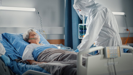 Hospital Coronavirus Emergency Department Ward: Team of Doctors wearing Coveralls, Face Masks Take Care of a Senior Patient Lying in Bed, Put Oxygenの写真素材