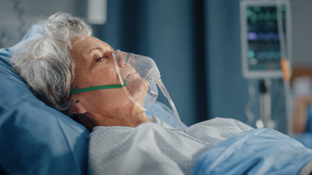 Hospital Ward: Portrait of Beautiful Elderly Woman Wearing Oxygen Mask Sleeping in Bed, Fully Recovering after Sickness and Successful Surgery. Seniorの写真素材