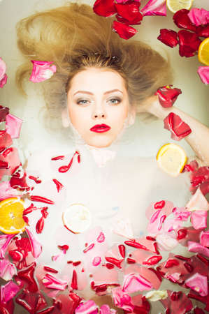 luxury spa queen: elegant blue eyes pinup girl with silk skin having fun laying in water bath & looking at camera relaxing on colorful copy space background, close up portraitの写真素材