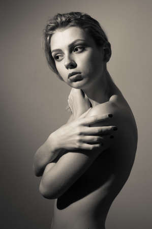 Beautiful young lady looking aside covering her shoulder standing posing on copy space , black and white portraitの写真素材