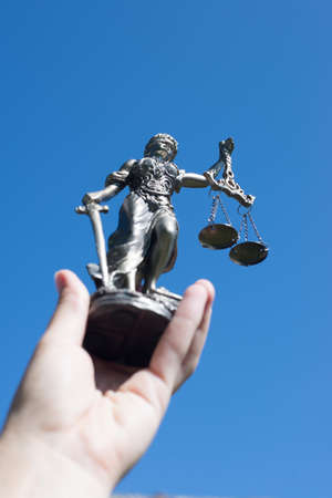 hand holding sculpture of themis, femida or justice goddess up in bright blue sky backgroundの写真素材
