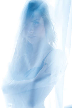 hiding behind curtain tulle seductive slim blond pretty lady having fun standing in bikini or undies happy smiling relaxing looking at camera over window light copy space background portrait closeupの写真素材