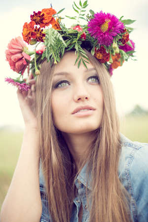 portrait of beautiful brunette young woman in marigold flower crown and pink lipstick makeup posing gracefully on green park bokeh outdoors copy space backgroundの写真素材